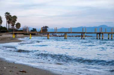 Arka planda deniz dalgaları ve iskelesi olan güzel bir deniz manzarası. Gün batımında arka planda bir rıhtım manzarası.