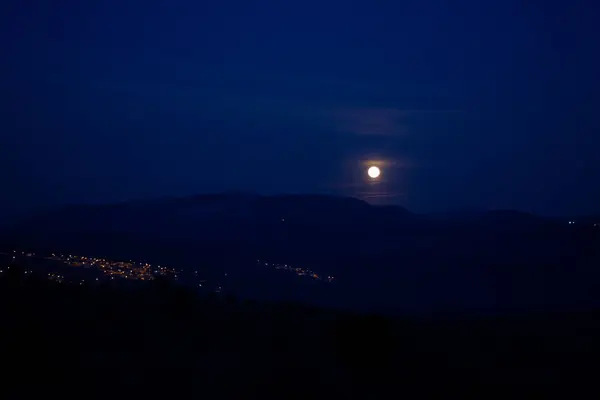 Gece dağ sırasının üzerinde dolunay var. Karanlık gecede dolunay fotoğrafları..