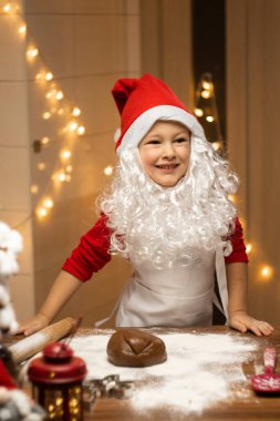 Noel Baba şapkalı, sakallı ve önlüklü sevimli çocuk Noel kurabiyesi hazırlıyor. Yüksek kalite fotoğraf