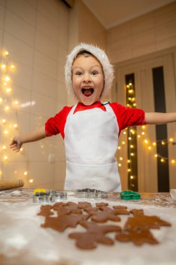 Noel Baba şapkalı küçük çocuk zencefilli kurabiye yapıyor. Noel ve Yeni Yıl gelenekleri. Noel pastanesi. İyi tatiller. Yüksek kalite fotoğraf