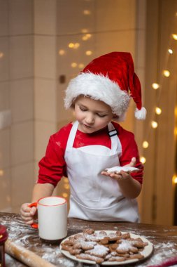 Noel zamanı. Noel kurabiyeleri yiyen ve yılbaşı süslemelerinde sıcak çay içen sevimli küçük çocuk. Kış tatili Yüksek kalite fotoğraf