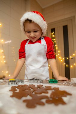 Noel ışıklarının yanındaki ahşap bir masada Noel kurabiyesi yapan tatlı çocuk. Noel yemeği konsepti. Yüksek kalite fotoğraf