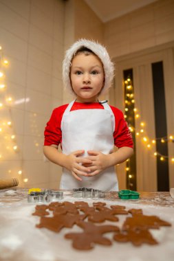 Noel Baba şapkalı küçük çocuk zencefilli kurabiye yapıyor. Noel ve Yeni Yıl gelenekleri. Noel pastanesi. İyi tatiller. Yüksek kalite fotoğraf