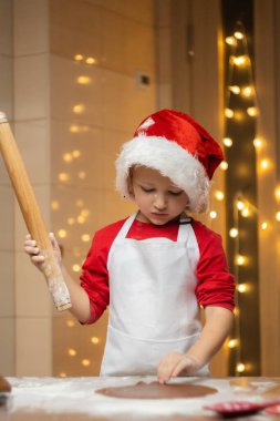 Çocuk şekilleniyor, masada hamur işindeki zencefilli adam şekline bürünüyor. Noel tatili için kurabiye pişirmeye hazırım. Hazırlık konsepti. Noel kurabiyesi pişiriyorum. Yüksek kalite fotoğraf