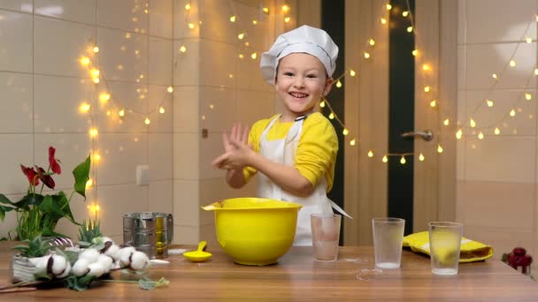 一个戴着帽子的蹒跚学步的厨师男孩从手中抖掉面粉 厨房里的孩子开玩笑地帮助做饭 家里厨房里的年轻助手高质量的4K镜头 — 图库视频影像