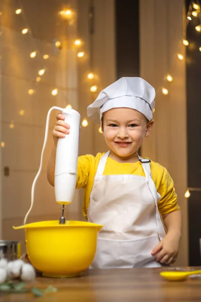 Little boy mixing cake ingredients in a mixing bowl whipping the flour and eggs to make the dough. High quality photo