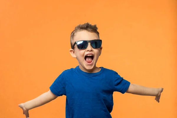Portrait of surprised cute little toddler boy in sunglasses. Child with open mouth having fun isolated over orange background. Looking at camera. Wow funny face. High quality photo