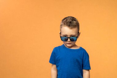 Sad kid wearing sunglasses posing on orange background. Summer, isolated, studio. Copy space. High quality photo