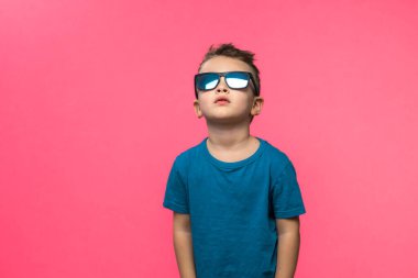 Little boy in sunglasses posing in studio on pink background. Copy space. High quality photo