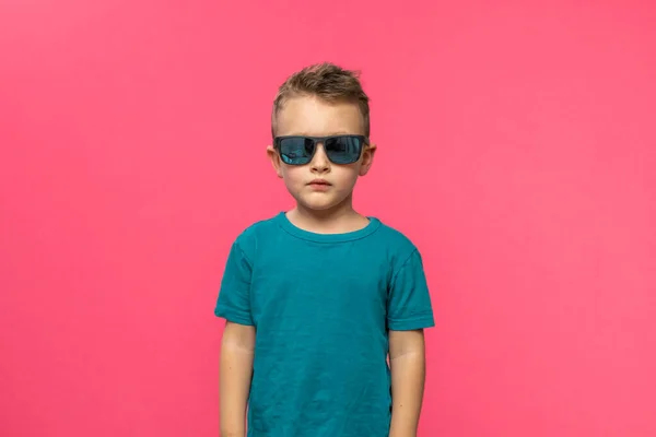 Little serious fashionable toddler boy in summer clothes and trendy sunglasses. Isolated on pink background. High quality photo