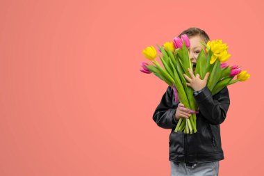 Anneler Günü 'nde büyük bir buket sarı ve pembe laleyle mutlu ve gülümseyen bir çocuk. Pembe arka planda güzel bir çocuğun portresi. Uzayı kopyala Yüksek kalite fotoğraf