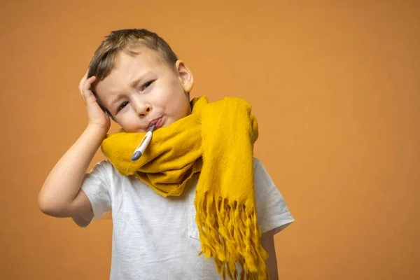 Little sick boy with Thermometer in mouth on orange background. High quality photo