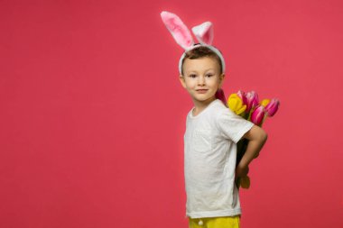 Cute funny kid with bunny ears, with a tulips in her hand on pink background. Easter greeting card. Copy space. High quality photo