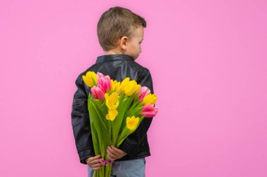 Boy hiding flowers of yellow and pink tulips behind itself, isolated on light pink background. High quality photo