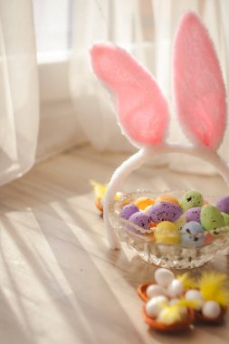 Renkli yumurtalar ve ahşap arka planda pembe Paskalya tavşanı kulakları olan cam bir tabak. Paskalya dini bayramı kavramı. Dikey fotoğraf. Yüksek kalite fotoğraf