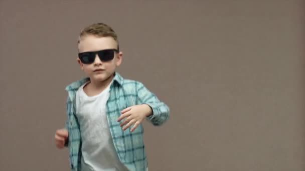 一个戴着太阳镜笑着的男孩手舞足蹈 在灰色背景下被隔离 高质量的4K镜头 — 图库视频影像