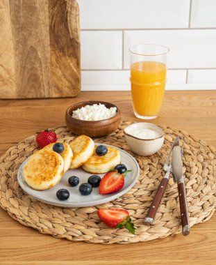 Peynirli kek ya da taze böğürtlenli süzme peynir, ekşi krema ve mutfak masasında portakal suyu. Sağlıklı ve lezzetli kahvaltı konsepti.