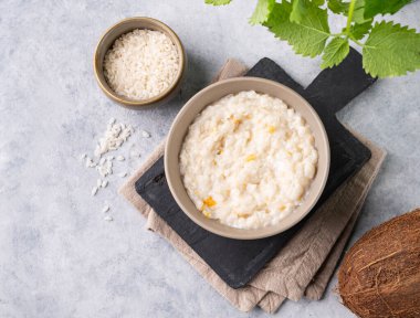 Meyveli pirinç lapası ve mavi arka planda hindistan cevizi sütü. Vejetaryen, lezzetli, besleyici ve sağlıklı kahvaltı kavramı. Üst görünüm ve kopyalama alanı.