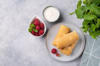 Ahududu ve ekşi kremalı ev yapımı krep. Mavi bir tabakta, hafif arkaplanda, taze naneli. Sağlıklı gıda konsepti. Üst görünüm ve kopyalama alanı.