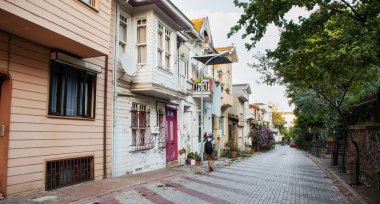 Sırt çantalı bir turist, eski bir yaz gününde eski renkli evlerle birlikte eski sokaklara bakıyor. Prenslerin Adaları, Türkiye.