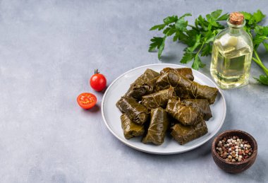 Dolma. Hafif arka planda zeytinyağı, domates ve biberli taze otlarla dolu mavi bir tabakta doldurulmuş üzüm yaprakları (geleneksel Kafkas, Türk, Yunan mutfağı). Boşluğu kopyala.