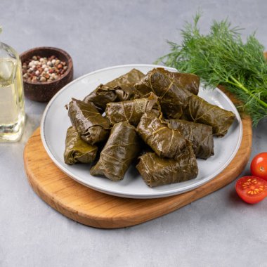Dolma. Mavi bir tabak üzerinde doldurulmuş üzüm yaprakları (geleneksel Kafkas, Türk, Yunan mutfağı) ve hafif bir zemin üzerinde taze otlar ve domateslerle tahta kesme. Boşluğu kopyala.