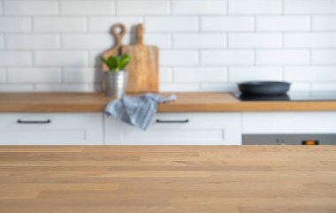 Wooden oak countertop with free space for mounting a product or layout against the background of a blurred white kitchen with plant and napkin. Copy space clipart