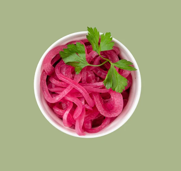 Pickled red onion rings in a white bowl with fresh herbs on green background. Healthy fermented food. Top view.