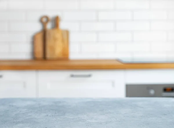 Wooden blue countertop with free space for mounting a product or layout against the background of a blurred white kitchen with cuting board. Horizontal orientation.