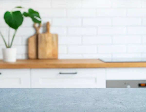 Wooden blue countertop with free space for mounting a product or layout against the background of a blurred white kitchen with cuting board and plant. Horizontal orientation.