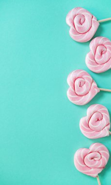 Yeşil arka planda kalp şeklinde pembe lolipoplar. Üst görünüm ve boşluk kopyala. Dikey yönelim.