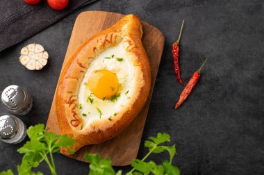 Adjarian khachapuri. Geleneksel Gürcü yemekleri, ahşap bir tahtada domatesli ve taze bitkisel peynirli ev yapımı ekmek ve yumurta sarısı ile yapılır. Üst görünüm ve kopyalama alanı.