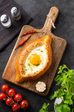 Adjarian Khachapuri yemeği. Geleneksel Gürcü yemekleri, ahşap bir tahtada domatesli ve taze bitkisel peynirli ev yapımı ekmek ve yumurta sarısı ile yapılır. Üst görünüm.