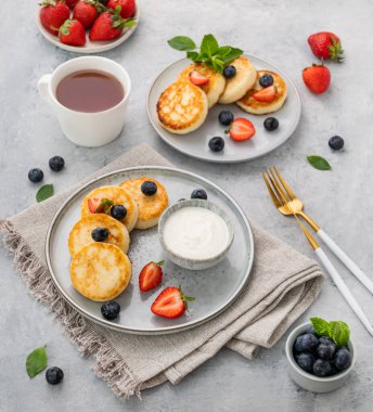 Süzme peynirli krep ya da taze blerryli şuruplu krep ve bir fincan çay eşliğinde gri arka planda ekşi krema. Sağlıklı ve lezzetli kahvaltı konsepti.