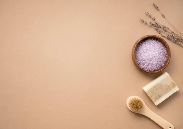 Flat lay organic sea salt for the body with dry lavender flowers, brush and soap  on a beige background. Skin care. The concept of a natural and eco-friendly spa product. Top view, copy space.