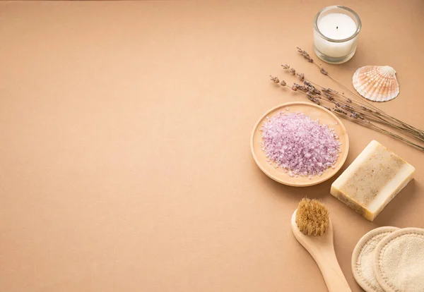 Organic sea salt for the body with dry lavender flowers, sponge, brush, soap and candle on a beige background. Skin care. The concept of a natural and eco-friendly spa product. Copy space.