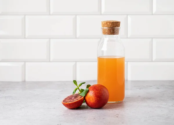 stock image Freshly squeezed orange juice in a bottle on the kitchen table with fresh red oranges. The concept of a healthy drink. Front view and copy   