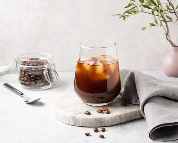 Iced coffee in a glass with ice cubes and grains on a light marble background. The concept of a cold summer drink.