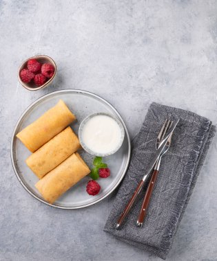 Peçeteli, arka planda hafif bir tabakta ahududu ve ekşi kremalı ev yapımı krep. Sağlıklı gıda konsepti. Üst görünüm ve kopyalama alanı.