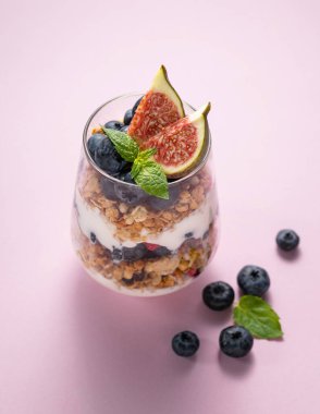 Tahıllı yoğurt, incir ve yaban mersinli pembe arka planda bir bardak. Sağlıklı ve besleyici bir kahvaltı. Diyet yemek. Üst görünüm ve kopyalama alanı.