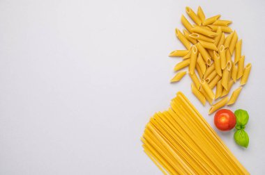 Gri arka planda farklı makarna tipleri var. Domates ve fesleğenli makarna. Üst görünüm ve kopyalama alanı.