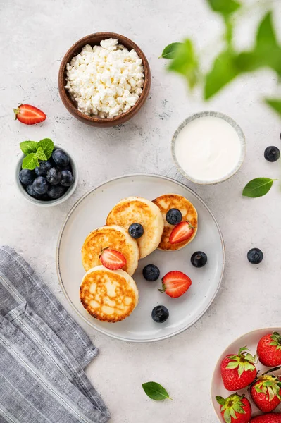 stock image Flat lay pancakes with cottage cheese with fresh blerries and sour cream on a gray background. The concept of a healthy and delicious morning breakfast. Top view.