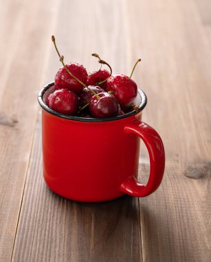 Güneşli bir yaz sabahında, koyu ahşap arka planda kırmızı bardakta taze kirazlar. Kırsal stil kavramı.