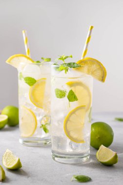 Taze limonla mojito içilir. Limon, limon, nane ve buzlu, gri arka planda uzun bir bardakta taze bir kokteyl. Yaz soğuk içecekler konsepti. Ön görünüm.