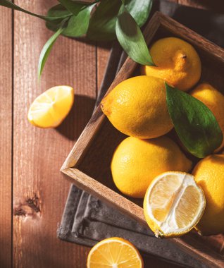 Tahta bir kutuda yaprakları olan taze limonlar. Taze sıkılmış limonata için turunçgil meyvesi. Koyu kompozisyon ve köy tarzı. Üst görünüm ve boyama resmi.