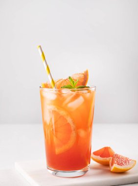 Buz, nane ve greyfurt dilimli taze greyfurt suyu beyaz mermer arka planda bir bardakta dilimlenmiş narenciye dilimleri yakın. Ön görünüm.