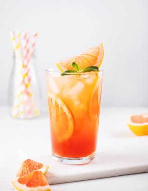 Buz, nane ve greyfurt dilimli taze greyfurt suyu beyaz mermer arka planda bir bardakta dilimlenmiş narenciye dilimleri ve kağıt tüplerle. Ön görünüm.