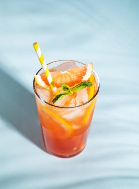 Taze greyfurt suyu, buzlu, naneli ve greyfurtlu. Mavi arka planda, gölgeli bir bardakta dilimlenmiş.. 