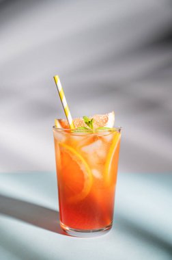 Taze greyfurt suyu, buzlu, naneli ve greyfurtlu. Mavi arka planda, gölgeli bir bardakta. Ön görünüm