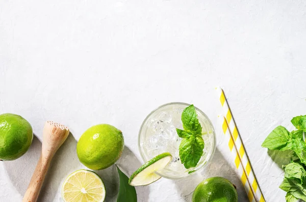 stock image Flat lay of mojito cocktail with lime, fresh mint and ice on white texture background. Summer refreshment citrus drink. Top view and copy space.